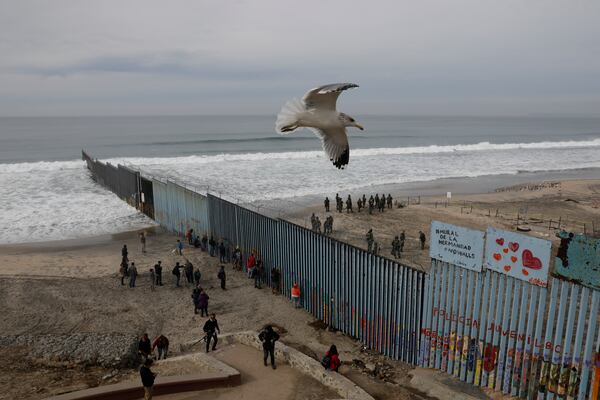 FILE - People peer through the border wall as U.S. Border Patrol in San Diego prepare for the arrival of hundreds of pro-migration protesters, in Tijuana, Mexico, Dec. 10, 2018. (AP Photo/Rebecca Blackwell, File)