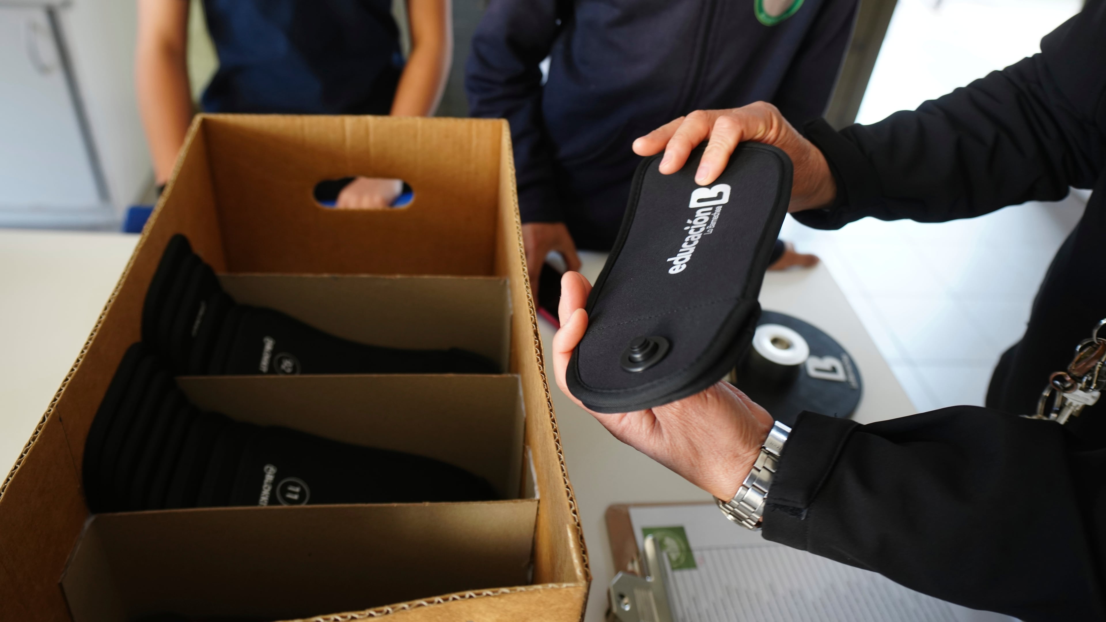 FILE - A professor passes out cell phone signal jammers to students to place their cell phones into, as part of a pilot program to reduce mobile use during school hours, at Bicentenario School in Santiago, Chile, Sept. 8, 2025. (AP Photo/Esteban Felix, File)