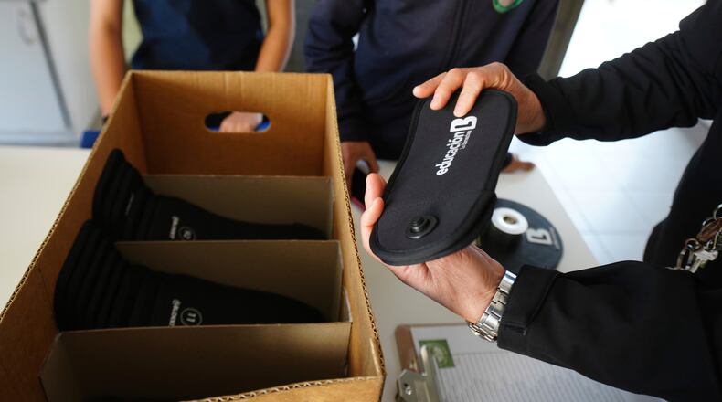 FILE - A professor passes out cell phone signal jammers to students to place their cell phones into, as part of a pilot program to reduce mobile use during school hours, at Bicentenario School in Santiago, Chile, Sept. 8, 2025. (AP Photo/Esteban Felix, File)
