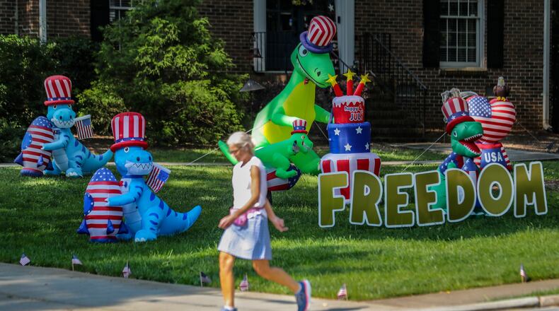 Alyson Cohen strolled by the display of dinosaurs on Dunwoody Club Drive near Braffington Court in Dunwoody on Friday, June 9, 2023. The display of dinosaurs first appeared in the neighborhood in 2020 then quickly evolved into holiday themed displays along with encouraging messages. (John Spink / John.Spink@ajc.com)