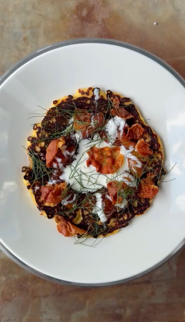 A large plate filled with a johnnycake and squash, topped with tomatoes and a creamy sauce, garnished with fresh herbs.