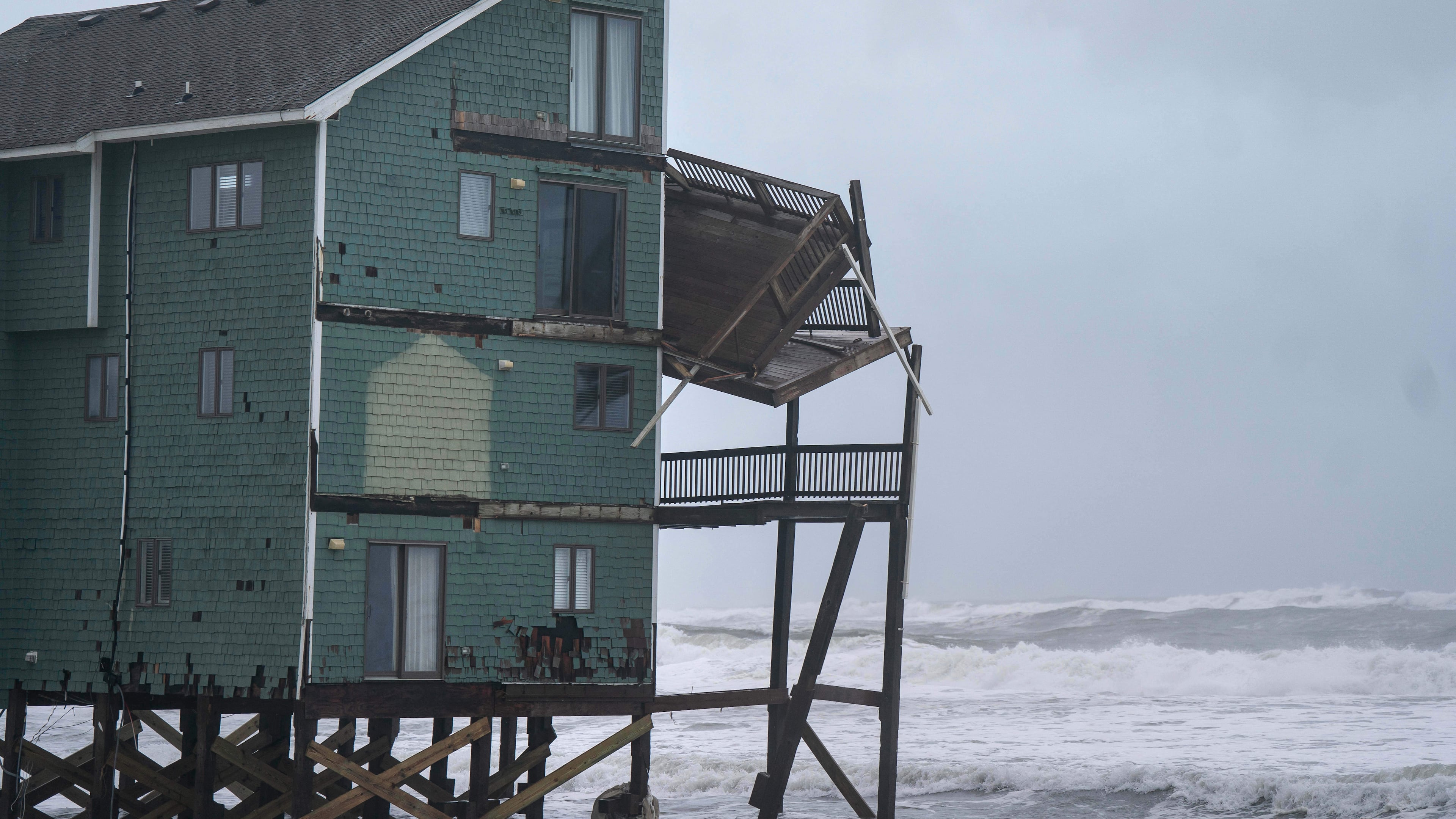A balcony hangs off a home at risk of collapse in the midst of a storm, Sunday, Oct. 12, 2025, in Buxton, N.C. (AP Photo/Allison Joyce)