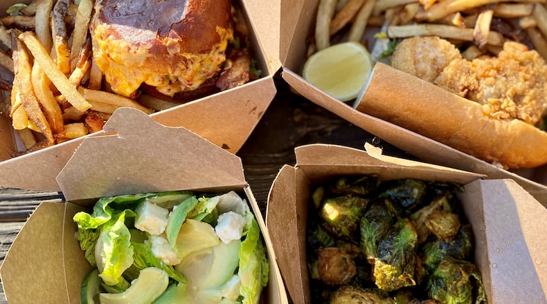 Takeout from Biggerstaff includes (clockwise from top left) the house burger with pimento cheese and bacon; the loaded seafood po’boy; crispy Brussels sprouts; and a gem salad. Wendell Brock for The Atlanta Journal-Constitution