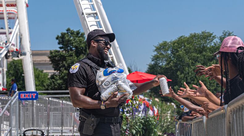 Children reach for cold bottles of water from U.S. National Park Police Officer R. Douglass as they wait in line for the ferris wheel at the Great American State Fair on the National Mall, Wednesday, July 1, 2026, in Washington. (AP Photo/Jen Golbeck)