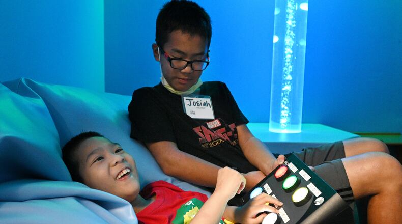 Summer camp participant Toby, 8, plays and learns using technology as his brother and volunteer Josiah, 12, assists in sensory room during a summer camp for children with special needs at Lekotek of Georgia in Tucker on Tuesday, July 12, 2022. Campers experience fun-filled, challenging activities that develop literacy, communication, fine motor, cognitive, and recreational abilities. Children with and without disabilities play and learn together in an environment that facilitates success. (Hyosub Shin / Hyosub.Shin@ajc.com)