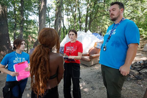 From left to right, Tracy Woodard from Intown Cares; Lauren Hopper, a street medicine nurse from Mercy Care; and Cody Wallace from Intown Cares provide outreach at the Cooper Street encampment on Monday, Aug. 12, 2014. They were helping someone schedule an appointment to visit a clinic. (Miguel Martinez / AJC)