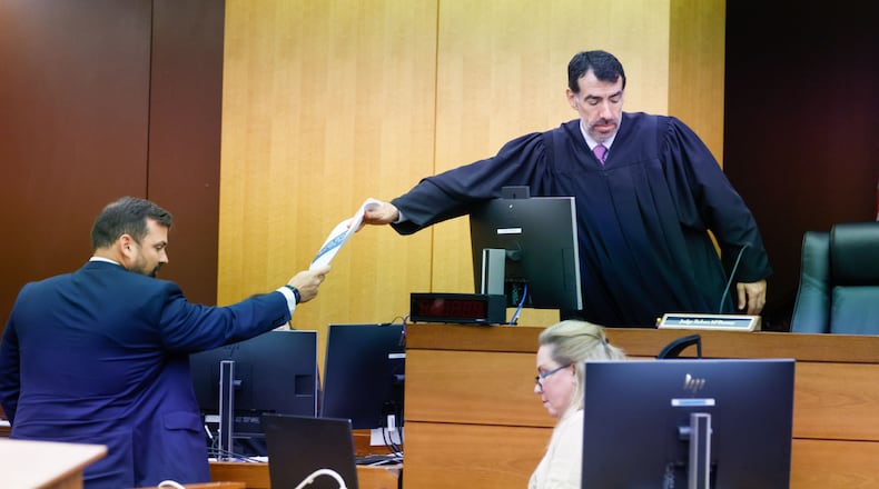 Baxter Drennon (left), a lawyer representing the Republican National Committee, hands documents to Fulton County Superior Court Judge Robert McBurney on Tuesday during a trial brought by the Georgia Democratic Party challenging the State Election Board’s certification rule. (Miguel Martinez/AJC)