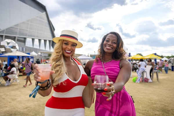Two women hold cups toward the camera In the grass outside of Mercedes-Benz Stadium in Atlanta.