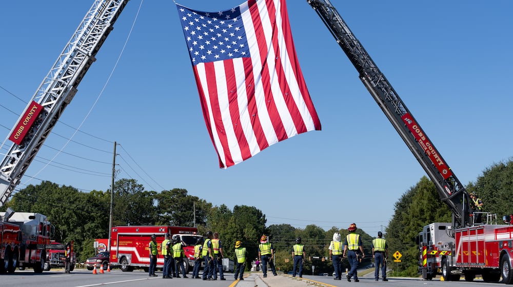 The Cobb County fire department hangs a U.S. flag from their fire trucks as a procession for fallen Dekalb County Firefighter Preston Fant arrives at West Cobb Funeral Home on Wednesday, Sept. 10, 2025. (Ben Hendren for the AJC)