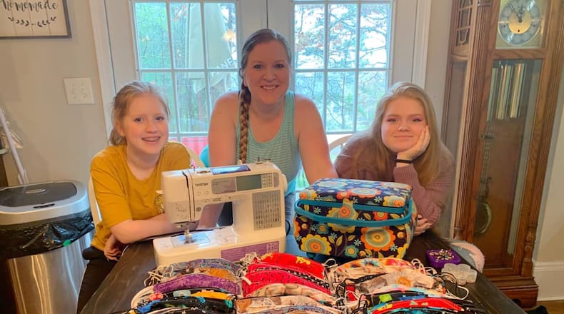Rebekah Gelatt Sharp and her daughters stand behind dozens of face masks sewn for area health-care workers. (Facebook)