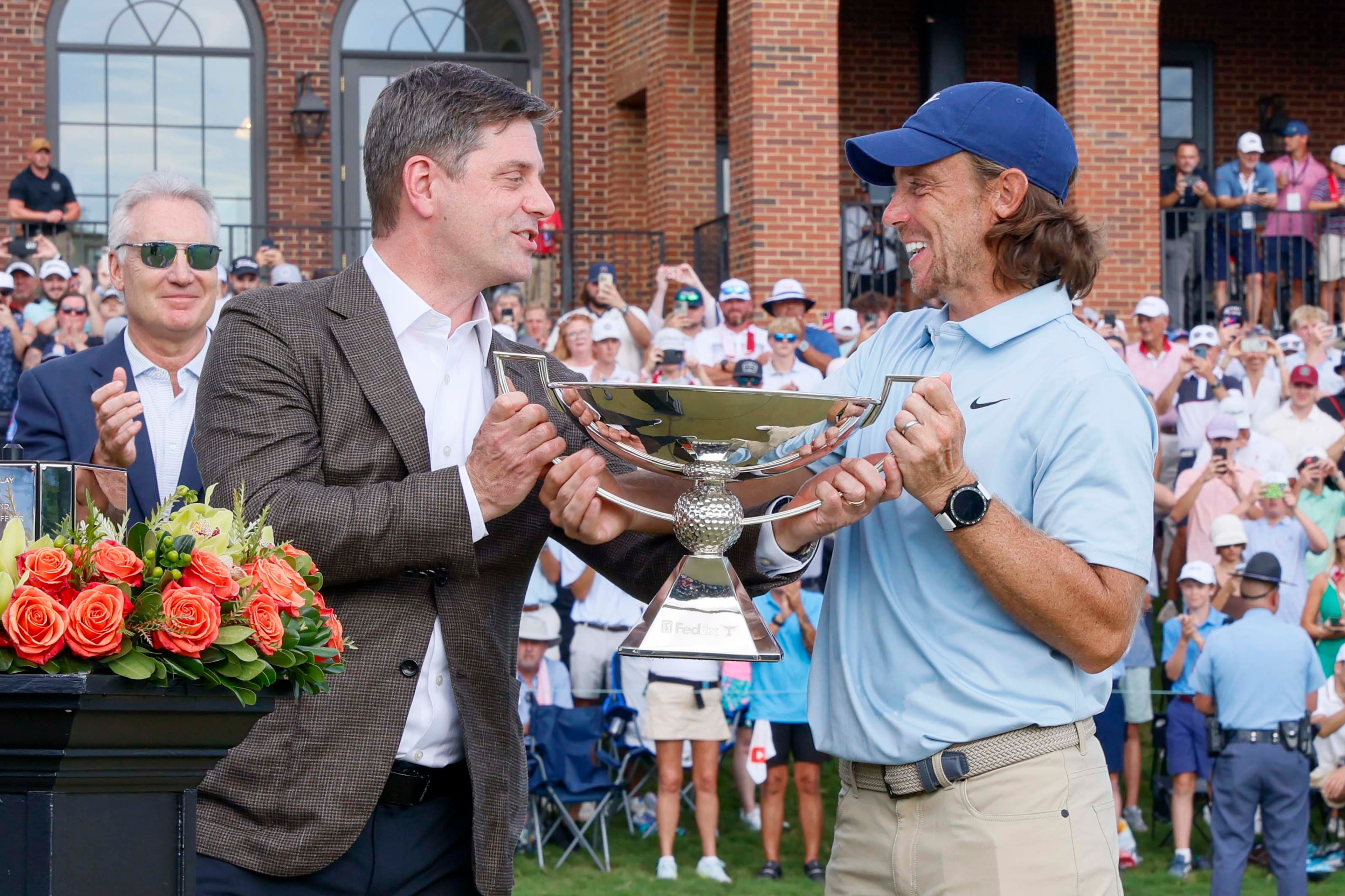 PGA Tour CEO Brian Rolapp presents the Tour Championship trophy to Tommy Fleetwood of England after his victory at the PGA Tour Championship at East Lake Golf Club on Sunday, Aug. 24, 2025, in Atlanta. (Miguel Martinez/ AJC)