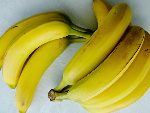 Two bunches of ripe yellow bananas with a few brown marks arranged on a white surface.