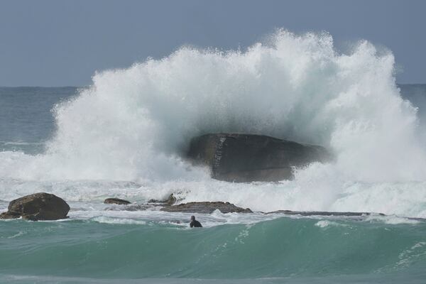 A surfer watches as a large wave hits a rock as large swells hit Sydney's Bondi Beach Wednesday, April 2, 2025. (AP Photo/Mark Baker)