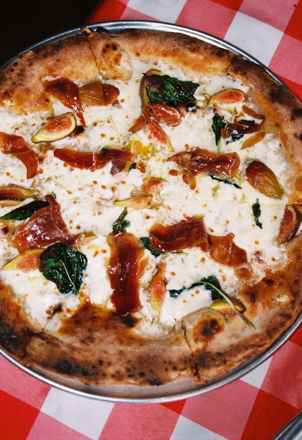 A close-up of a whole fig and duck pizza with a thicker crust on a checkered table cloth.