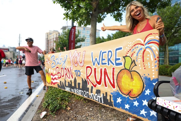 Spectator Shelia Loccisano (right) holds a sign as she cheers on runners on Hope Hill during the Peachtree Road Race on Saturday, July 4, 2026, in Atlanta. (Estela Muñoz/AJC)