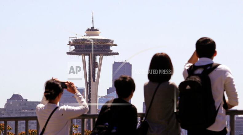 Tourists look across at the Space Needle, where a floor of scaffolding remains below the upper portion, in Seattle on Tuesday, May 22, 2018. The family-owned landmark is set to unveil the biggest renovation in its 56-year history next month, a $100 million investment in a single year of construction that transformed the structure's top viewing level some 500-feet above ground. (AP Photo/Elaine Thompson)