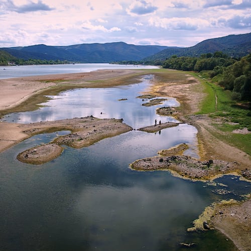 People walk on sandbanks exposed by record-low water levels in the Danube River after drought and extreme heat near Nagymaros, Hungary, on Aug. 18, 2026. (AP Photo/Bela Szandelszky)