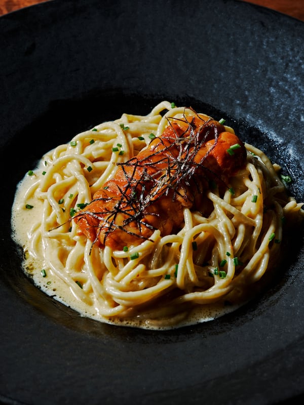 long pasta noodles topped with uni sit in a dark bowl
