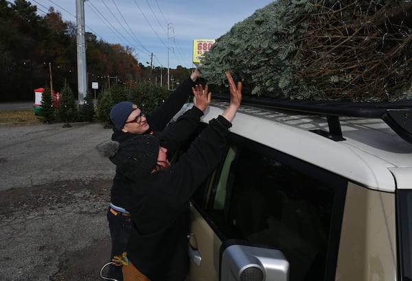 Rachel Quiggins (right) loads a Christmas tree on the top of customer Eric Vincent’s car at Tradition Trees.