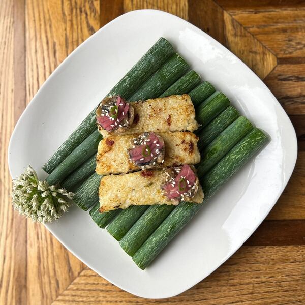 A plate with three slices of turnip cake garnished with chili crisp pickled herring. The turnip cakes are artfully presented on top of what looks like green onion stalks, with a floral garn
