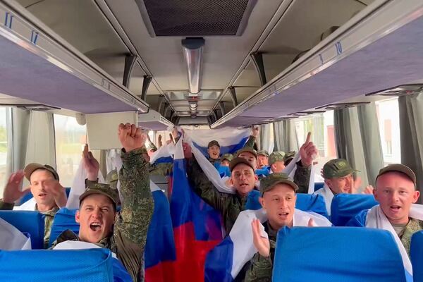In this photo taken from a video distributed by Russian Defense Ministry Press Service on Friday, June 20, 2025, Russian servicemen wave Russian national flags sitting in a bus at an exchange area in Belarus after returning from captivity during a POWs exchange of a group of servicemen between Russia and Ukraine. (Russian Defense Ministry Press Service via AP)