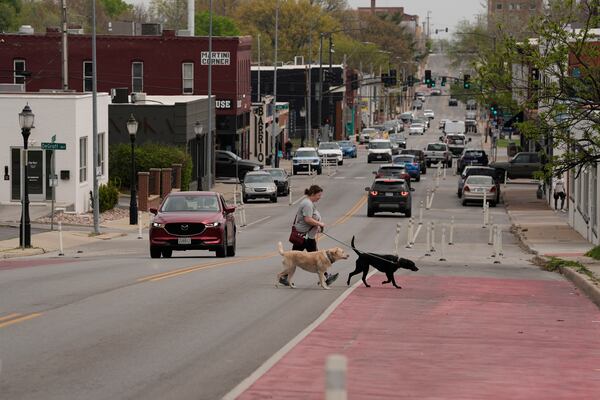 A woman and her dogs cross 31st Street in Kansas City, Mo., where the city implemented a "road diet" reducing the street from four lanes to two in an effort to reduce speeding and accidents, Thursday, April 17, 2025. (AP Photo/Charlie Riedel)