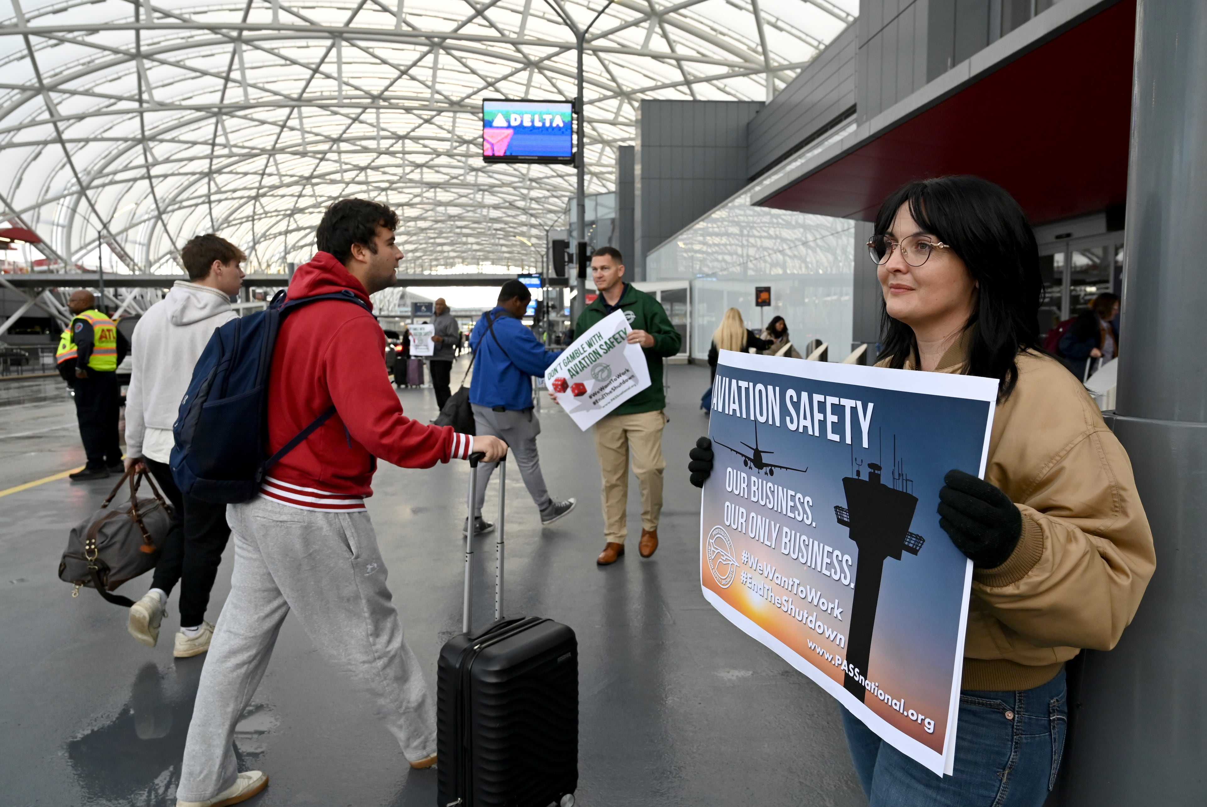 Amanda James (right), a union representative for PASS, holds a sign as airport travelers walk by at Hartsfield-Jackson Atlanta International Airport, Wednesday, October 29, 2025, in Atlanta. (Hyosub Shin/AJC)