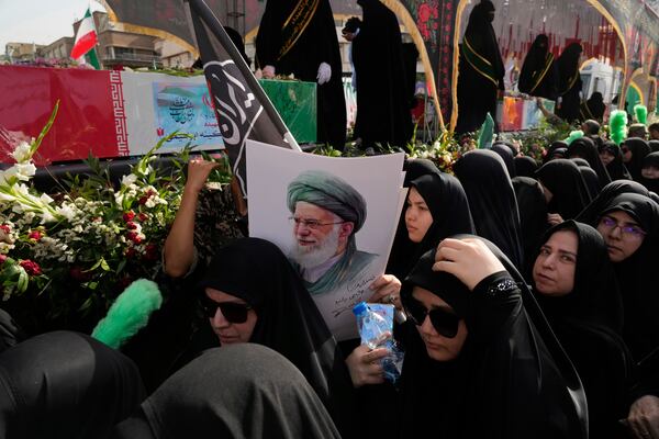 Mourners gather around the flag-draped coffins of the Iranian armed forces generals, nuclear scientists and their family members who were killed in Israeli strikes, during their funeral ceremony as one of them holds a poster of the Supreme Leader Ayatollah Ali Khamenei, in Tehran, Iran, Saturday, June 28, 2025. (AP Photo/Vahid Salemi)