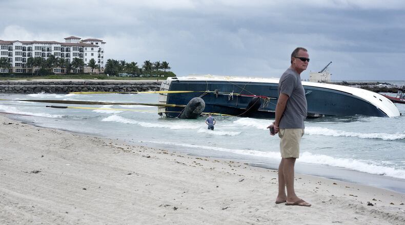 Yacht owner Thomas Baker stands on the beach as the salvage company employees work on towing his yacht ashore earlier this month. (Melanie Bell / Daily News)