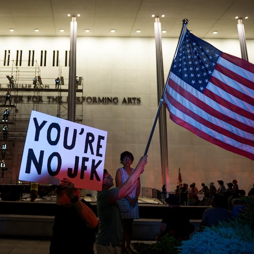 Protestors wave a U.S. and signs as workers prepare to remove President Donald Trump's name from the John F. Kennedy Center for the Performing Arts in Washington, Saturday, June 13, 2026. (AP Photo/Cliff Owen)