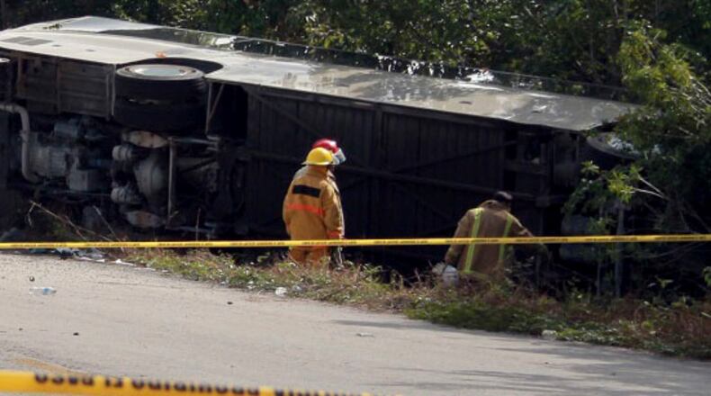 An ambulance sits parked next to an overturned bus in Mahahual, Quintana Roo state, Mexico, Tuesday, Dec. 19, 2017. The bus carrying cruise ship passengers to the Mayan ruins at Chacchoben in eastern Mexico flipped over on a highway early Tuesday. (Novedades de Quintana Roo via AP)