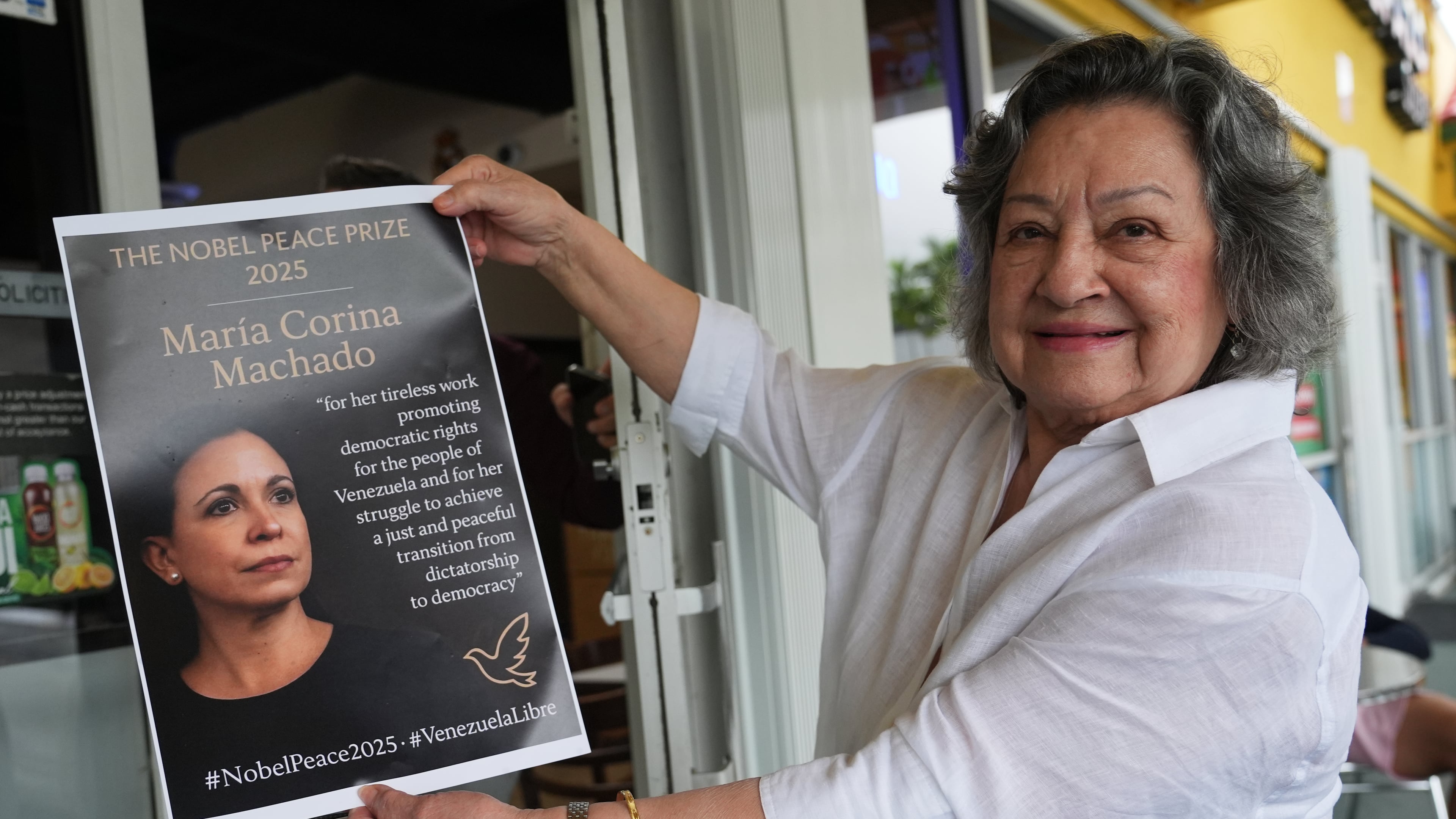 Iris Wilthew holds a poster in support of Venezuelan opposition leader Maria Corina Machado winning the Nobel Peace Prize, Friday, Oct. 10, 2025, in Doral, Fla. (AP Photo/Lynne Sladky)