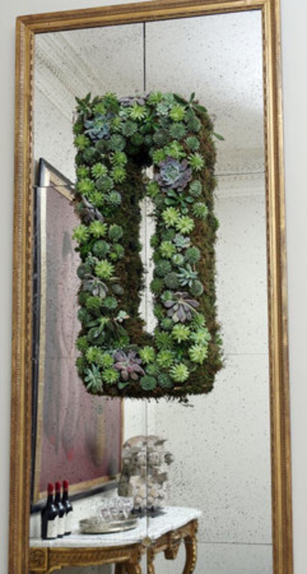 A rectangular wreath made of succulents accentuates the shape of an antique mirror.
