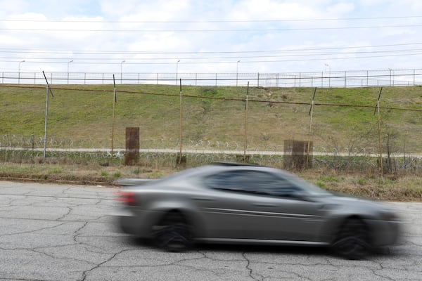 A car passes the patched fence at the prison camp. (David Barnes / For the AJC)