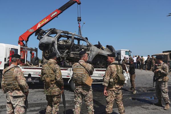 Lebanese army soldiers stand guard as workers use a crane to remove a charred car that was hit by an Israeli strike, in the southern coastal town of Ghazieh, Lebanon, Friday, April 18, 2025. (AP Photo/Mohammed Zaatari)