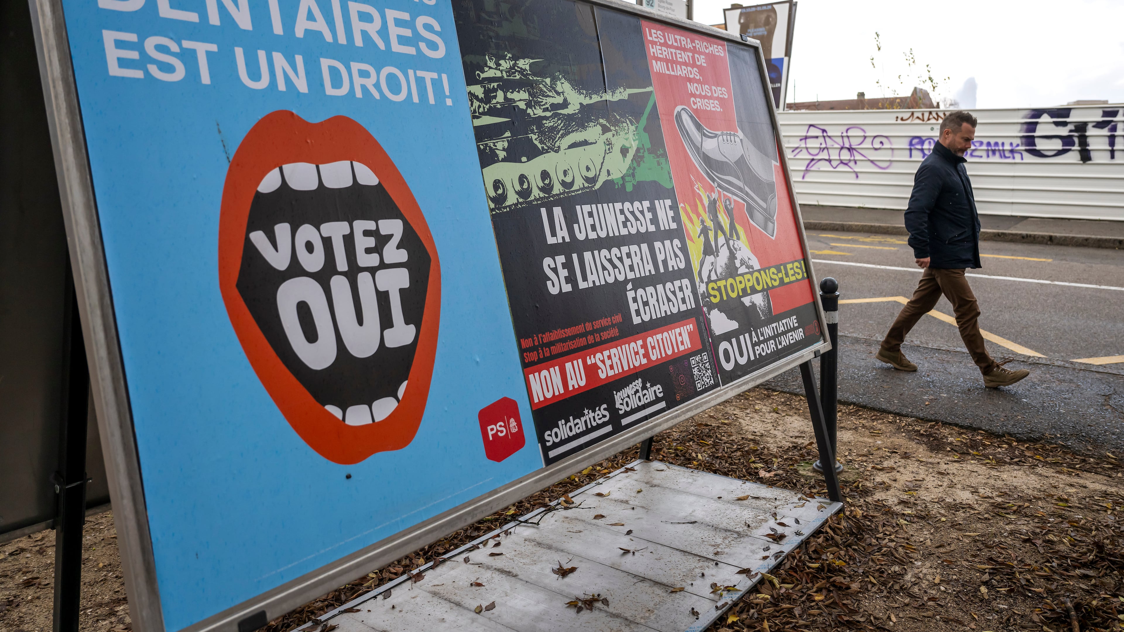 A person walks past referendum posters of political parties and associations as Swiss voters are casting ballots to decide whether women, like men, must do national service in the military, civil protection teams or in other forms, in Geneva, Switzerland, on Nov. 26, 2025. (Martial Trezzini/Keystone via AP)