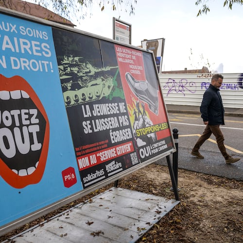 A person walks past referendum posters of political parties and associations as Swiss voters are casting ballots to decide whether women, like men, must do national service in the military, civil protection teams or in other forms, in Geneva, Switzerland, on Nov. 26, 2025. (Martial Trezzini/Keystone via AP)