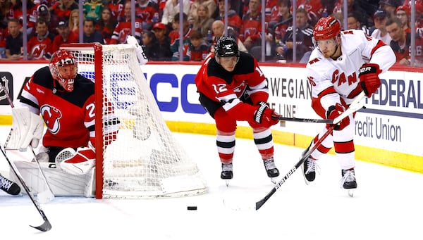 Carolina Hurricanes center Jack Roslovic (96) passes the puck against New Jersey Devils center Cody Glass (12) and goalie Jacob Markstrom (25) during the second period of Game 3 of a first-round NHL hockey playoff series Friday, April 25, 2025, in Newark, N.J. (AP Photo/Noah K. Murray)