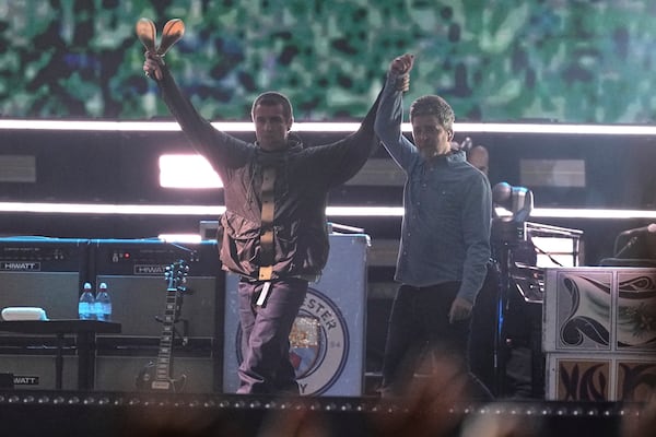 Liam Gallagher, left, holds the hand aloft of Noel Gallagher from the band Oasis as they perform during their reunion concert on Friday, July 4, 2025, in Cardiff. (Photo by Scott A Garfitt/Invision/AP)