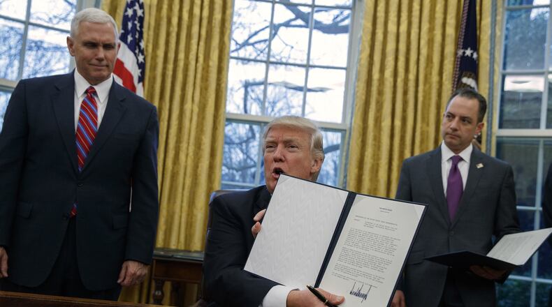 In this Jan. 23, 2017, photo, Vice President Mike Pence, left, and White House Chief of Staff Reince Priebus watch as President Donald Trump shows off an executive order to withdraw the U.S. from the 12-nation Trans-Pacific Partnership trade pact agreed to under the Obama administration in the Oval Office of the White House in Washington. (AP Photo/Evan Vucci)