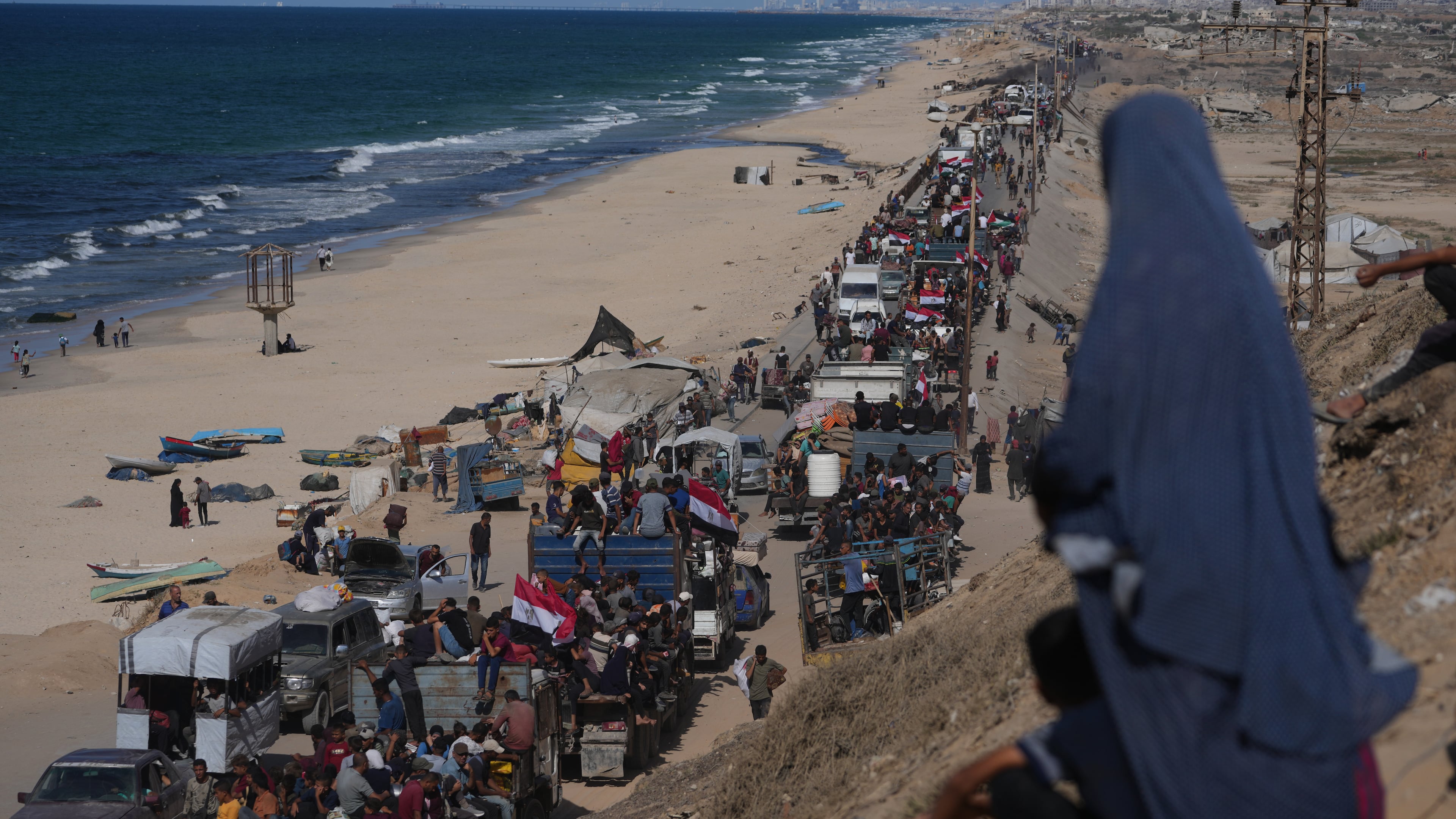 Displaced Palestinians ride on trucks loaded with belongings and wave Egyptian and Palestinian flags as they travel along the coastal road near Wadi Gaza in the central Gaza Strip, moving toward Gaza city, Saturday, Oct. 11, 2025, after Israel and Hamas agreed to a pause in their war and the release of the remaining hostages. (AP Photo/Jehad Alshrafi)