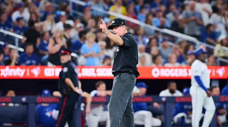Umpire Chris Guccione, center, announces a rules check during an umpire review during the seventh inning of a baseball game between the Toronto Blue Jays and the Boston Red Sox in Toronto, Monday, Aug. 10, 2026. (Sammy Kogan/The Canadian Press via AP)