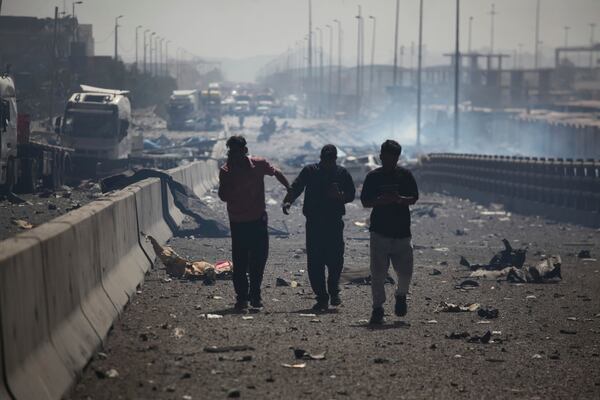 In this photo provided by Islamic Republic News Agency, IRNA, men walk through debris after a massive explosion rocked a port near the southern port city of Bandar Abbas, Iran, Saturday, April 26, 2025. (Mohammad Rasoul Moradi/IRNA via AP)