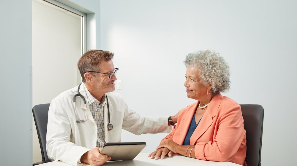 Male doctor is engaged in discussion with senior female patient, sitting at table in doctor office