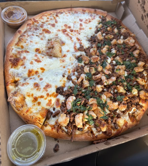 A large pizza in a pizza box, with half topped with only cheese and half topped with carne asada and cilantro