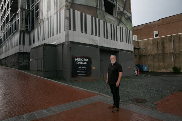 Charlottesville, Virginia, resident and journalist David McNair stands in front of John Dewberry's undeveloped property on Water Street in Charlottesville, which remains covered by a mural called "Music Box on Main" that was installed in February 2022. (Kirsten Luce for the AJC)
