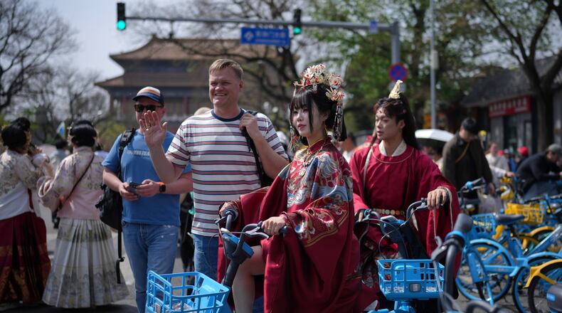 A foreign tourist poses next to a Chinese couple dressed in imperial costumes near the Forbidden City, in Beijing, on Sunday, April 12, 2026. (AP Photo/Andy Wong)