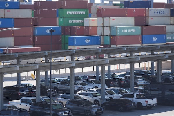 Vehicles are parked under solar panels as shipping containers sit stacked at the Long Beach Container Terminal in Long Beach, Calif., on Tuesday, April 8, 2025. (AP Photo/Damian Dovarganes)
