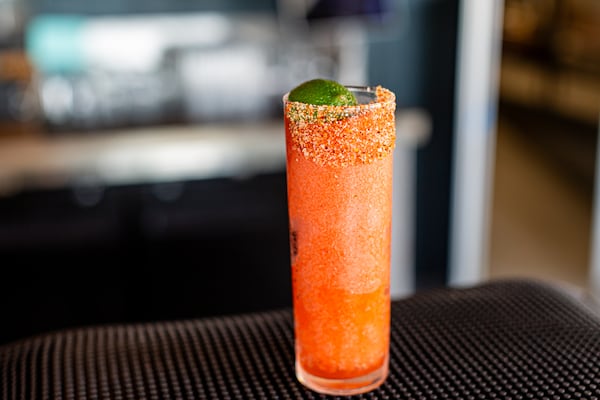 A brightly colored frozen cocktail in a tall Collins glass on a dark tabletop.