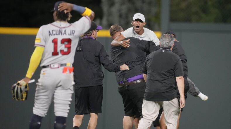 Field guards haul away one of two fans who approached Atlanta Braves right fielder Ronald Acuna Jr. (13) before the bottom of the seventh inning of a baseball game against the Colorado Rockies, Monday, Aug. 28, 2023, in Denver (AP Photo/David Zalubowski)